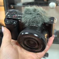 در سال‌های اخیر بازار دوربین‌های دست دوم به یکی از بخش‌های پویای عکاسی حرفه‌ای و نیمه‌حرفه‌ای تبدیل شده است. با رشد قیمت تجهیزات عکاسی و ورود مدل‌های جدید سونی به بازار جهانی، بسیاری از کاربران ترجیح می‌دهند به جای خرید محصول نو، به‌سراغ گزینه‌های کارکرده اما سالم بروند. در این میان، برند سونی با تنوع گسترده در سری‌های Alpha، Cyber-shot و ZV، بخش قابل‌توجهی از بازار را در اختیار دارد. اما خرید دوربین دست دوم، به‌ویژه در مدل‌های سونی که حساسیت بالایی دارند، نیازمند دقت، دانش فنی و تجربه عملی است. در این مقاله قصد داریم به‌صورت کاملاً تخصصی، فرآیند ارزیابی سلامت دوربین سونی دست دوم را بررسی کنیم؛ از وضعیت بدنه و عملکرد شاتر گرفته تا تست سنسور، منوها، درگاه‌ها و حتی تاریخچه استفاده کاربر قبلی. اهمیت شناخت وضعیت دوربین‌های دست دوم سونی دوربین‌های سونی به‌دلیل کیفیت ساخت بالا و طول عمر مکانیکی زیاد، معمولاً دوام قابل‌توجهی دارند؛ اما همان‌طور که هر وسیله الکترونیکی دیگری در معرض استهلاک است، این دوربین‌ها نیز در گذر زمان ممکن است دچار مشکلات فنی یا فیزیکی شوند. آگاهی از وضعیت واقعی یک دوربین دست دوم نه‌تنها از ضرر مالی جلوگیری می‌کند بلکه باعث می‌شود کاربر بداند چه میزان از ظرفیت فنی و اپتیکی دستگاه باقی مانده است. نکته کلیدی در خرید دوربین دست دوم سونی این است که ظاهر فریبنده همیشه تضمین‌کننده سلامت فنی نیست. ممکن است بدنه کاملاً تمیز باشد، اما شاتر بیش از حد کار کرده باشد یا سنسور در اثر گردوغبار و رطوبت آسیب دیده باشد. شناخت این نشانه‌ها و تشخیص دقیق سلامت دستگاه نیازمند نگاه تحلیلی و آزمون‌های عملی است. بررسی سلامت بدنه؛ از کیفیت ظاهری تا دوام ساختاری اولین گام در خرید دوربین سونی دست دوم، بررسی دقیق بدنه است. بدنه‌های سری Alpha معمولاً از آلیاژ منیزیم ساخته می‌شوند که مقاومت بالایی در برابر ضربه و حرارت دارد. با این حال، در اثر استفاده مکرر یا حمل‌ونقل نادرست ممکن است آثار خراش، فرورفتگی یا شکستگی در قسمت‌های خاصی مانند گوشه‌ها یا محل اتصال لنز مشاهده شود. در هنگام بررسی، باید به پیچ‌ها، دکمه‌ها، و درب‌های محفظه باتری و کارت حافظه دقت کرد؛ هرگونه لق‌زدگی یا تغییر رنگ در این نواحی می‌تواند نشانه باز شدن یا تعمیر قبلی دستگاه باشد. همچنین بررسی سلامت مانت لنز اهمیت بالایی دارد. مانت دوربین‌های سونی از نوع E یا A-mount است و هرگونه لقی در محل اتصال لنز می‌تواند بر فوکوس و انتقال داده تأثیر بگذارد. لمس سطح بدنه و تست مقاومت فیزیکی در برابر فشار ملایم، از روش‌هایی است که متخصصان برای تشخیص آسیب‌های ساختاری استفاده می‌کنند. شاتر و عمر مفید آن؛ معیار اصلی سلامت فنی شاتر مکانیکی یکی از حیاتی‌ترین اجزای هر دوربین است و در دوربین‌های سونی نیز نقش کلیدی دارد. هر دوربین دارای عمر مفید مشخصی برای شاتر است که بسته به مدل می‌تواند بین ۲۰۰ تا ۵۰۰ هزار شات متغیر باشد. در هنگام خرید دوربین دست دوم، اطلاع از تعداد شات واقعی یکی از مهم‌ترین مراحل است. این عدد معمولاً در فایل EXIF عکس‌ها ذخیره می‌شود و با نرم‌افزارهای تخصصی قابل بررسی است. دوربینی که ظاهر خوبی دارد اما تعداد شات آن بسیار بالا است، عملاً نزدیک به پایان عمر مفید شاتر قرار دارد. علاوه بر این، صدای شاتر نیز باید مورد توجه قرار گیرد؛ اگر صدای باز و بسته شدن بیش از حد بلند، ناهماهنگ یا همراه با تاخیر است، ممکن است شاتر نیاز به سرویس یا تعویض داشته باشد. در مدل‌هایی مثل Sony A7 III یا A9 II که از شاترهای هیبریدی (مکانیکی و الکترونیکی) بهره می‌برند، بررسی هر دو حالت الزامی است. سلامت سنسور؛ قلب تصویربرداری دیجیتال سنسور در دوربین‌های سونی، به‌ویژه در مدل‌های فول‌فریم و APS-C، گران‌ترین و حساس‌ترین قطعه محسوب می‌شود. کوچک‌ترین خراش، لکه، یا گردوغبار روی سنسور می‌تواند کیفیت تصویر را به‌شدت کاهش دهد. برای بررسی وضعیت سنسور، باید دوربین را روی دیافراگم بسته (مثلاً f/16) قرار داد و از سطحی یکنواخت مانند آسمان یا دیوار سفید عکس گرفت. سپس با زوم کردن روی تصویر، می‌توان نقاط تیره یا خطوط غیرعادی را تشخیص داد. در صورت مشاهده لکه‌های متعدد، احتمال آلودگی یا آسیب سطحی وجود دارد. سنسورهای Exmor R و Exmor RS سونی به‌دلیل فناوری Back-Illuminated ساختار پیچیده‌ای دارند و تعمیر یا تعویض آن‌ها هزینه‌بر است. بنابراین سلامت سنسور، تعیین‌کننده اصلی ارزش واقعی دوربین دست دوم است. تست عملکرد فوکوس، نمایشگر و منوها یکی دیگر از مراحل حیاتی، ارزیابی عملکرد فوکوس خودکار است. دوربین‌های سونی با سیستم‌های فوکوس پیچیده‌ای مانند Real-time Eye AF و Fast Hybrid AF شناخته می‌شوند. هنگام خرید دوربین دست دوم، باید بررسی کرد که آیا فوکوس همچنان سریع، دقیق و بدون خطا عمل می‌کند یا خیر. در برخی موارد ممکن است ماژول فوکوس در اثر ضربه یا نفوذ رطوبت دچار خطا شود. نمایشگر لمسی نیز باید از نظر دقت رنگ، روشنایی و پاسخ‌گویی به لمس بررسی شود. پیکسل سوخته، نقاط نورانی یا سایه‌های ثابت روی نمایشگر می‌توانند نشانه نقص سخت‌افزاری باشند. همچنین لازم است وارد منوی تنظیمات شوید و از درستی عملکرد دکمه‌ها، پیچ‌های کنترلی، درگاه‌های HDMI، USB و ورودی میکروفون اطمینان حاصل کنید. ارزیابی تاریخچه استفاده و اطمینان از اصالت دستگاه یکی از خطاهای رایج خریداران دوربین دست دوم سونی، اعتماد بیش از حد به ظاهر دستگاه است. گاهی اوقات دوربین‌ها از مناطق مرطوب یا شرایط کاری دشوار به بازار فروش مجدد راه می‌یابند. بررسی برگه خرید، شماره سریال بدنه و مقایسه آن با اطلاعات نمایش‌داده‌شده در منو، راهی مطمئن برای اطمینان از اصالت کالا است. شماره سریال حک‌شده بر روی بدنه باید با داده‌های داخلی دستگاه هم‌خوانی داشته باشد. در صورتی که فروشنده از ارائه اطلاعات خرید یا فاکتور امتناع کند، احتمال قاچاقی بودن یا تعمیر سنگین وجود دارد. استفاده از کارت حافظه و باتری اصلی سونی نیز یکی از نشانه‌های نگهداری صحیح دستگاه است. نکات پایانی و جمع‌بندی تحلیلی خرید دوربین سونی دست دوم اگر با دقت و دانش انجام شود، می‌تواند تجربه‌ای بسیار ارزشمند و اقتصادی باشد. بسیاری از عکاسان حرفه‌ای با انتخاب مدل‌های کارکرده اما سالم، به ابزارهایی با کیفیت بالا و قیمت مناسب دست یافته‌اند. با این حال، بی‌توجهی به جزئیات فنی مانند تعداد شات، سلامت سنسور و اصالت بدنه می‌تواند به ضرر مالی قابل‌توجهی منجر شود. انتخاب بین مدل‌های پرطرفدار مانند A7 III، A6400 یا ZV-E10 باید با توجه به نوع کاربرد انجام شود. برای مثال، اگر تمرکز شما بر فیلم‌برداری و تولید محتواست، سلامت سیستم فوکوس و درگاه‌های ورودی اهمیت بیشتری دارد، در حالی که برای عکاسی حرفه‌ای، سنسور و شاتر اهمیت حیاتی دارند. در نهایت، بهترین راه اطمینان از خرید موفق، آزمایش حضوری دستگاه پیش از پرداخت وجه است. اگر امکان تست حضوری وجود ندارد، خرید از نمایندگی‌های معتبر سونی مانند اطمینان کمرا در ایران، گزینه‌ای امن‌تر و قابل‌اعتمادتر است، زیرا این مراکز دستگاه‌ها را از نظر فنی بررسی و گارانتی سلامت ارائه می‌کنند.